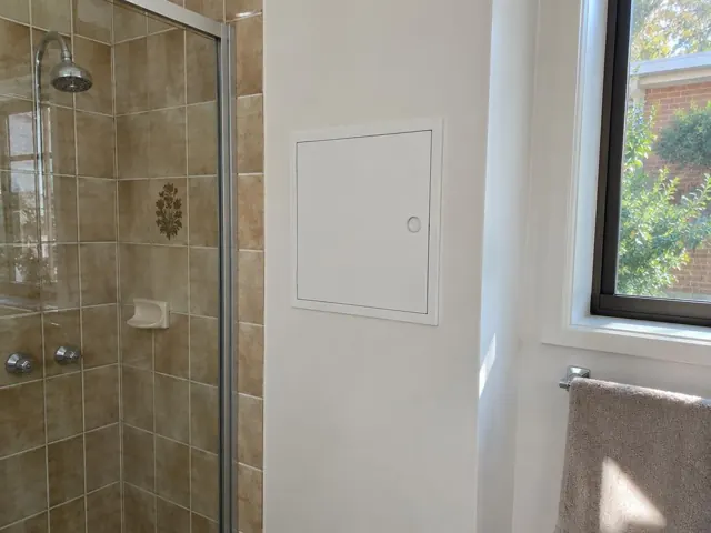 Bathroom shower wall with small white access panel beside a window in a tiled bathroom in Sutherland