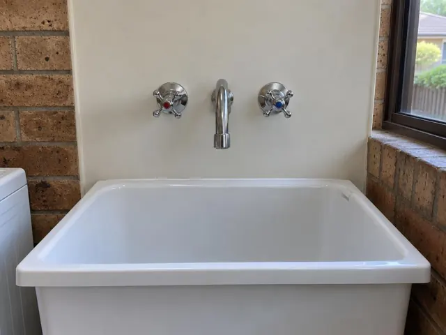White laundry sink with a chrome mixer tap and twin wall taps against a painted wall in Kirrawee